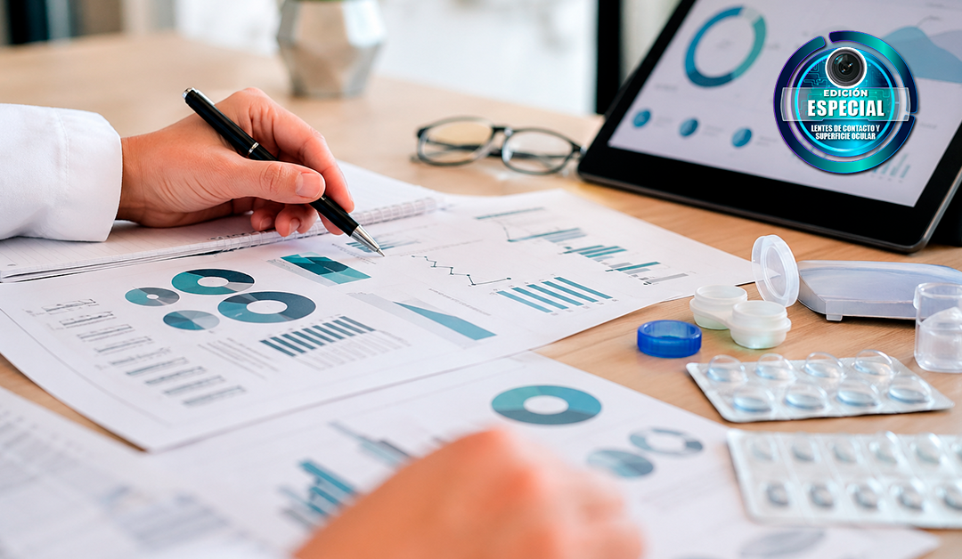 Person analyzes charts and graphs on a desk, writing with a pen while a tablet shows graphs nearby.