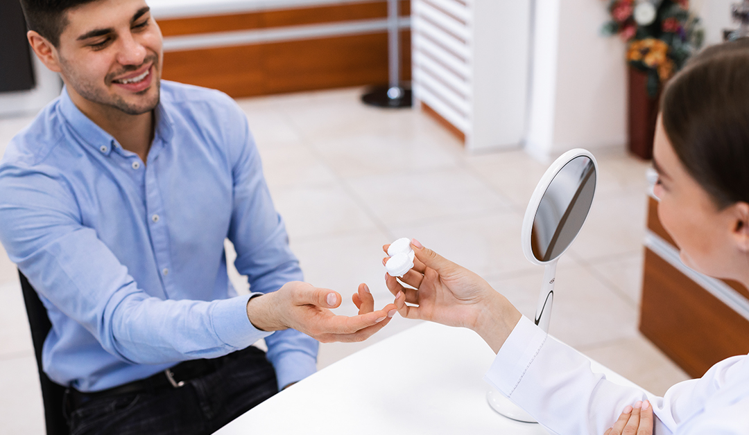 Man in a blue shirt receives two small white items from a clinician at a reception desk, both smiling.