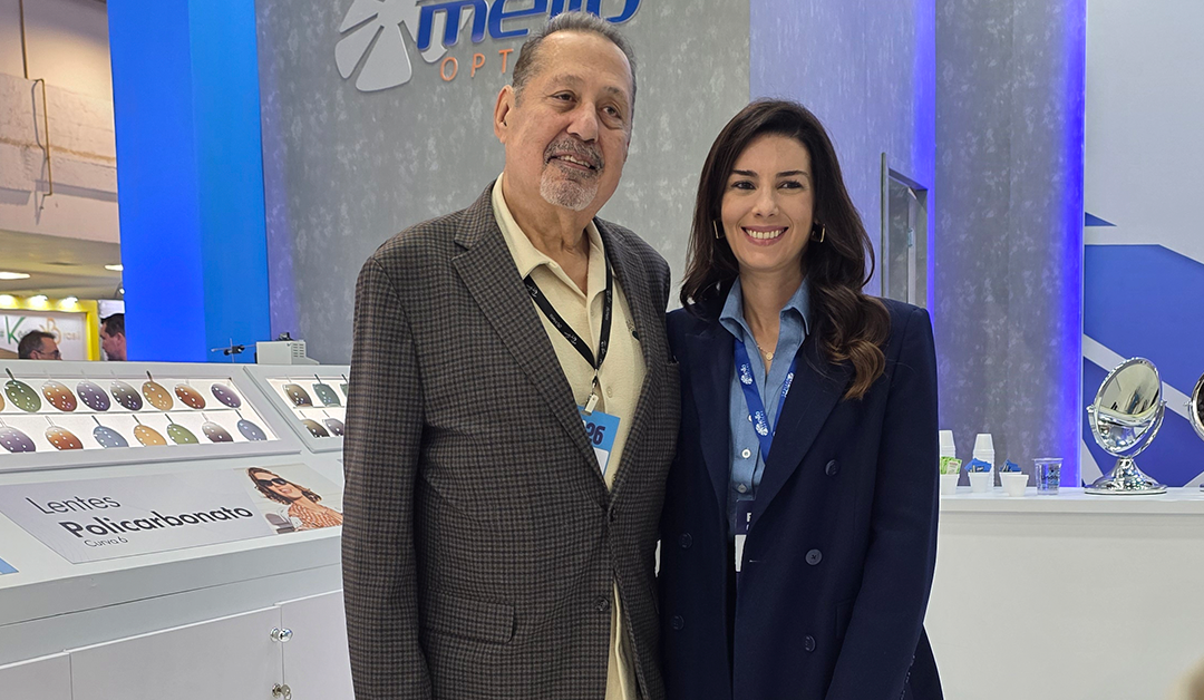 Two smiling professionals posing at an eyewear booth displaying lenses, with a 'Lentes Policarbonato' sign in the background.