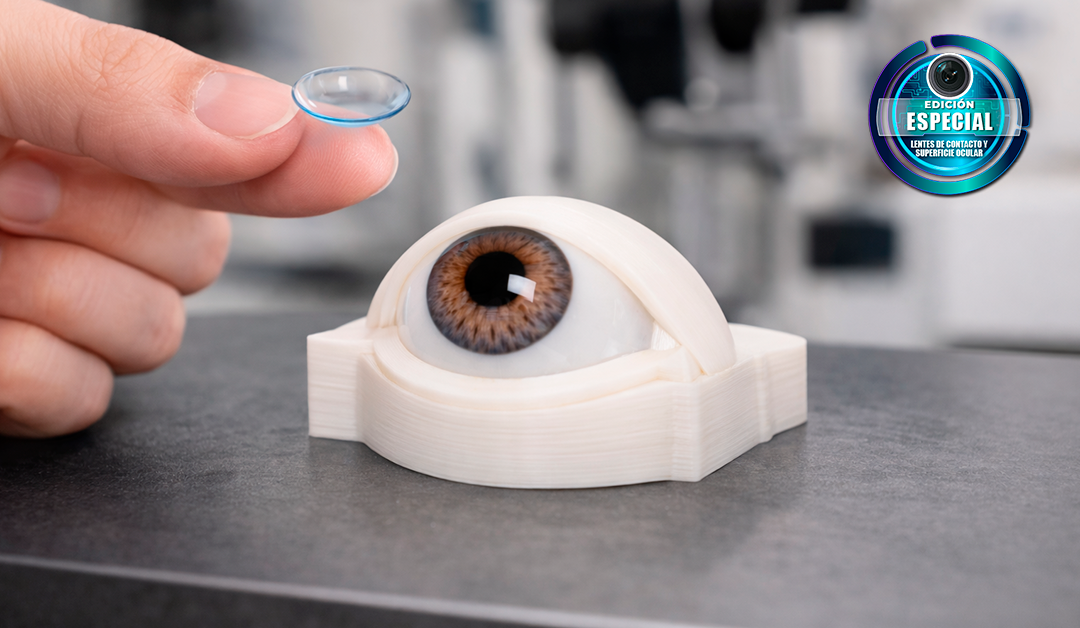 3D-printed eye model on a lab bench as a fingertip holds a contact lens above it for fitting.