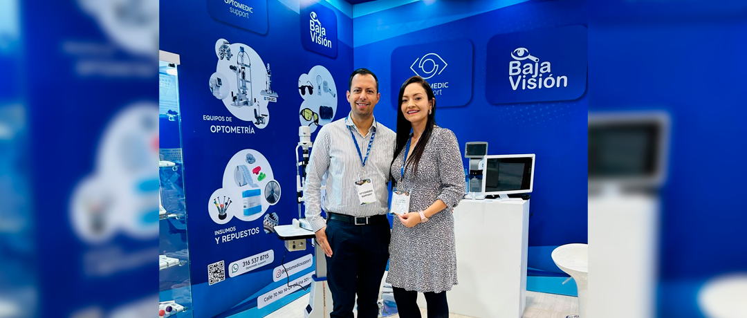 Two professionals pose at a Baja Visión trade show booth featuring optometry equipment and blue branding.