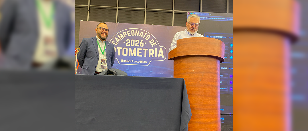 Two men on a conference stage; one stands behind a wooden podium as the other smiles beside a blue banner reading 'Campeonato 2026 Autometría'.