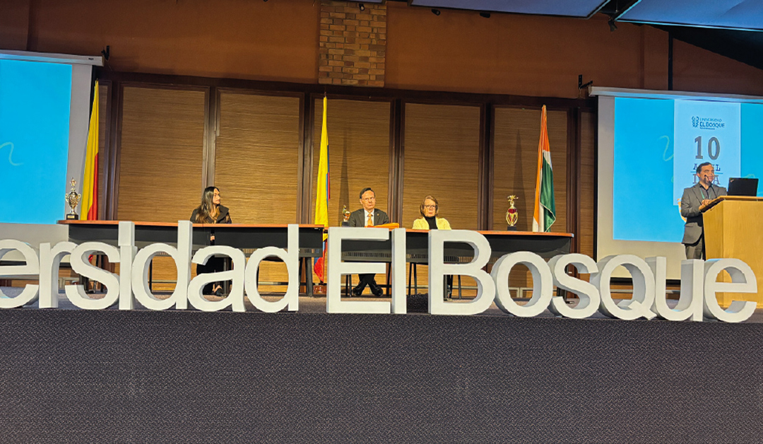 Panel discussion on a stage with four panelists behind a long table; large white letters spell 'Universidad El Bosque' in front.