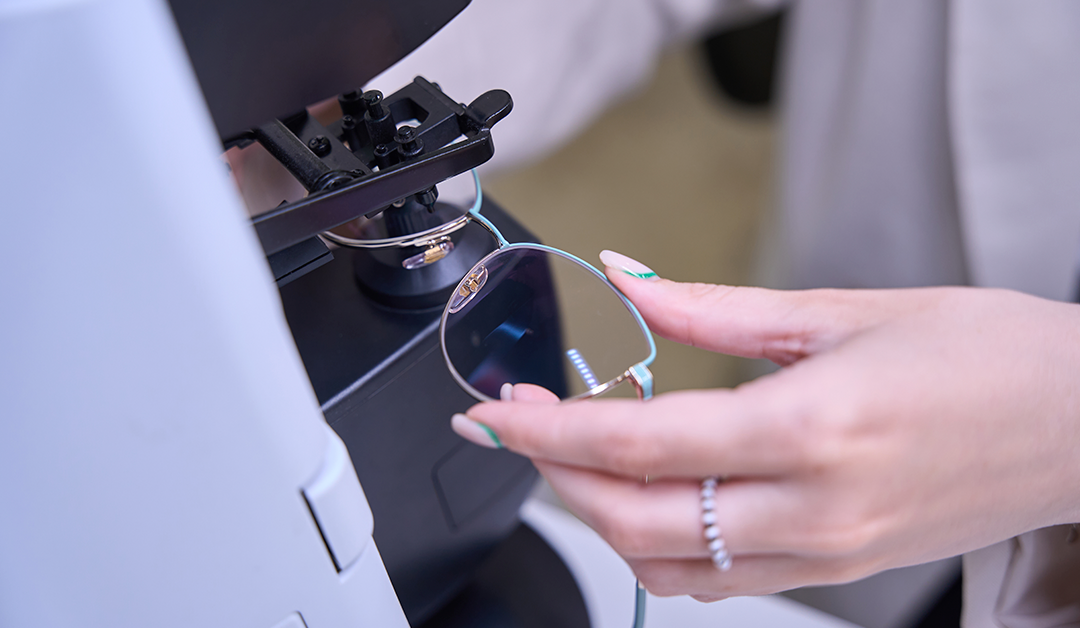 Close-up of hands aligning a circular eyeglass lens with an optical testing instrument in a lab item set-up.