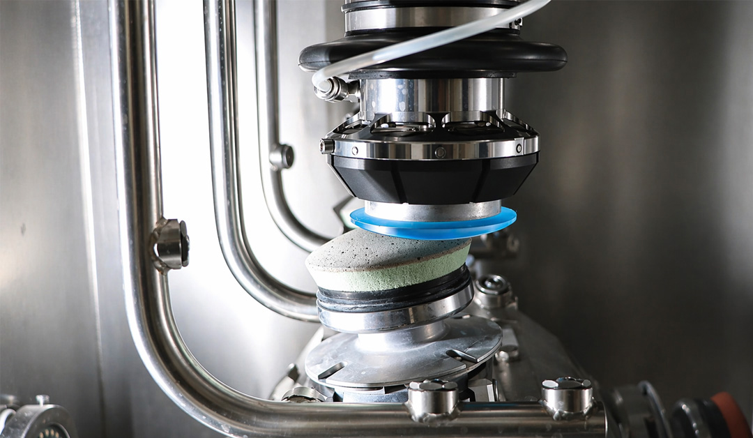 Close-up of a stainless steel industrial grinding/polishing head with an abrasive wheel and blue spacer inside a metal chamber.