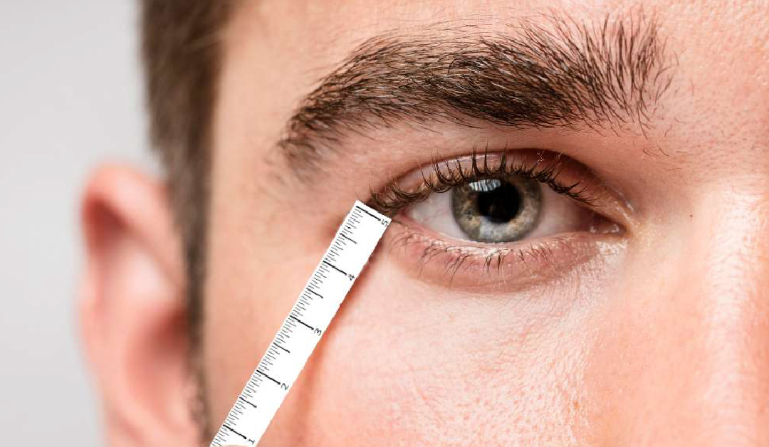 Close-up of a man's eye with a ruler pressed along the lower eyelid to measure the eye area.