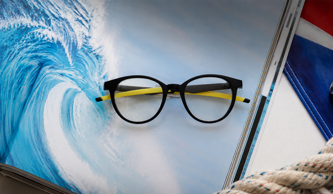 Black round eyeglasses with yellow temples resting on a surf magazine page showing a breaking wave?