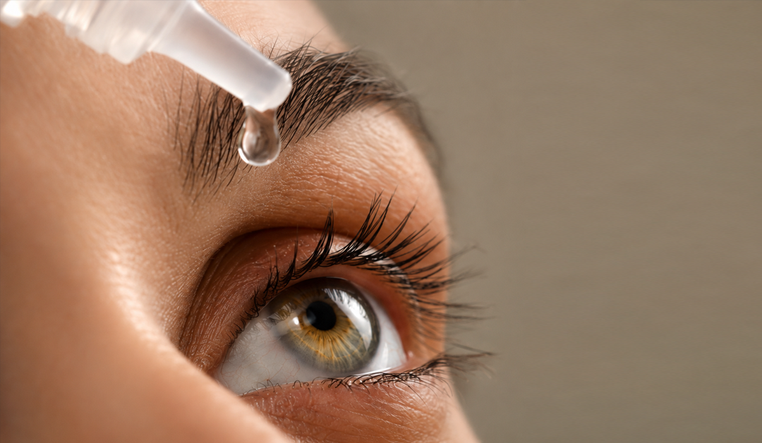 Close-up of an eye as a dropper releases a medicine drop toward the eye outdoors or in a clinical setting.
