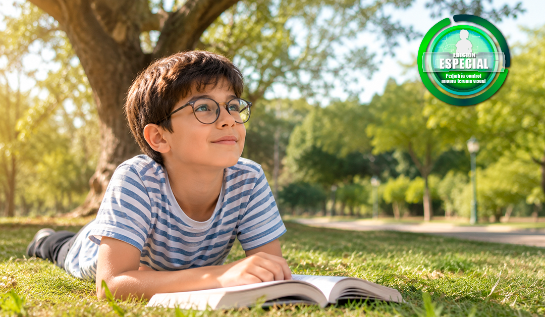 Boy with glasses lying on the grass in a park, reading an open book as sunlight filters through trees; a green circular logo sits in the top-right corner.