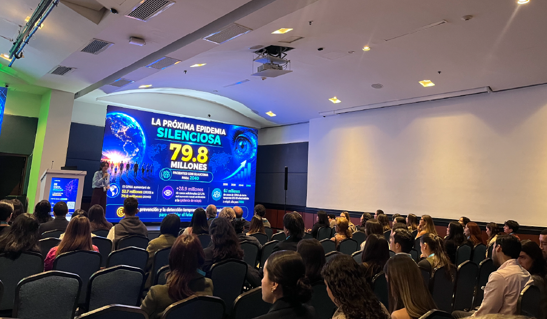 Speaker presenting in a lecture hall with a large screen showing 'La próxima epidemia silenciosa 79.8 millones' and an audience of students or professionals in rows of chairs.