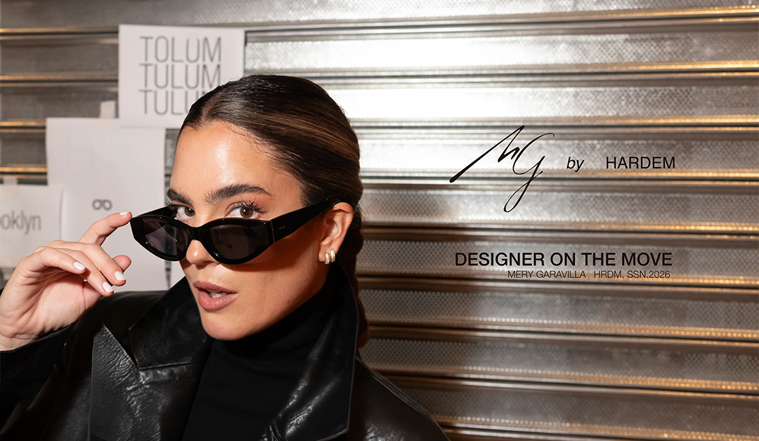 Stylish woman in a black leather jacket adjusts narrow black sunglasses against a metallic backdrop with fashion branding behind her.