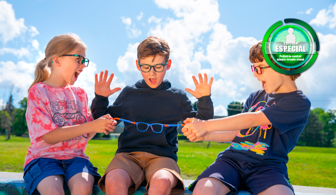 Three children outdoors on a sunny day, stretching a blue glasses frame between them and laughing together with arms raised in excitement.