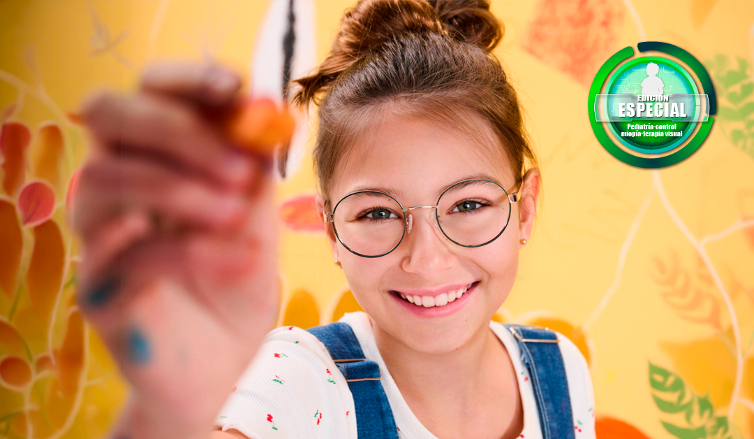 Smiling girl with round glasses reaches toward the camera, holding an orange marker in a bright, colorful mural background.