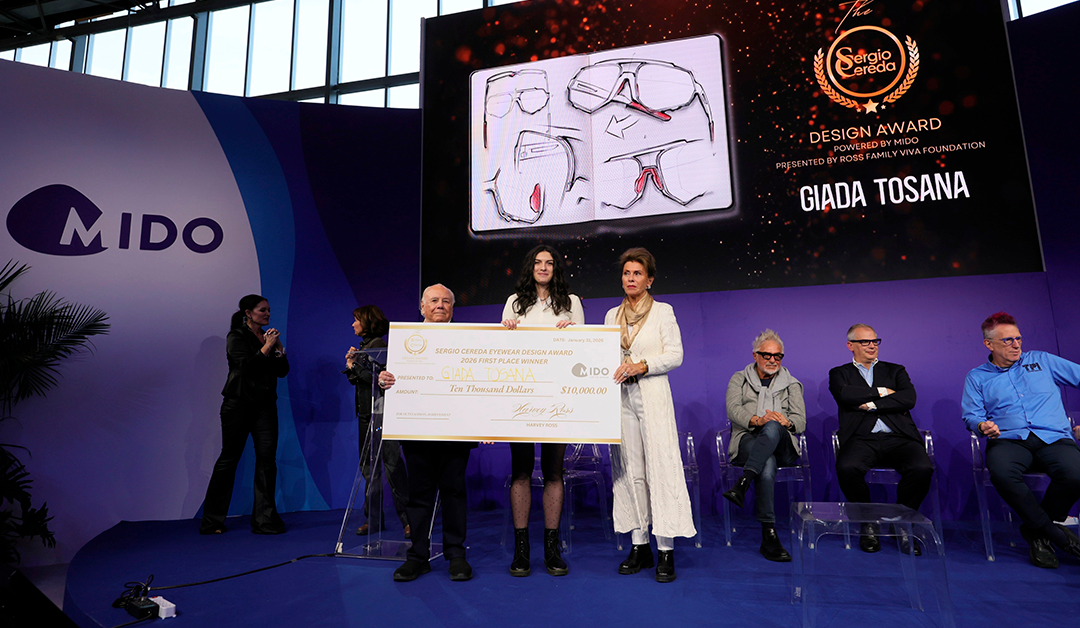 Award ceremony on a purple stage as three people hold a large ceremonial check for $10,000; a big screen and MIDO logo behind them show the event branding.