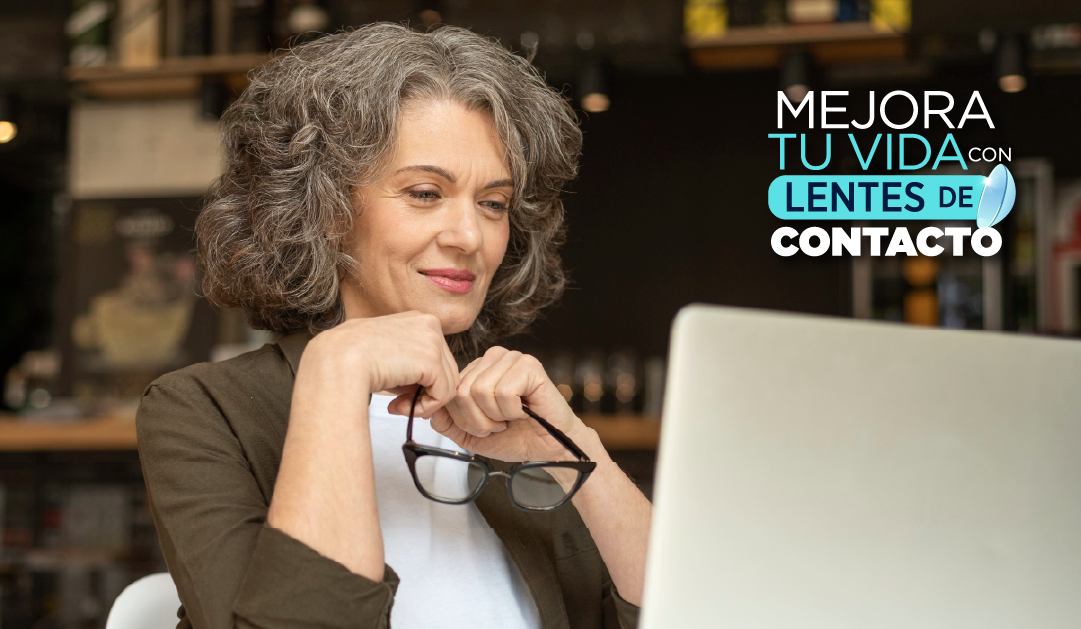 Mujer mayor con cabello rizado sosteniendo gafas y mirando una computadora; anuncio de lentes de contacto en la esquina superior derecha.