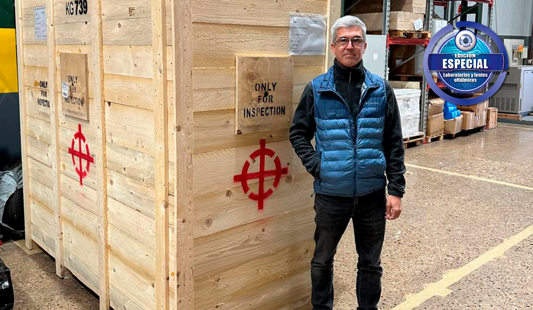 Man in a blue puffer vest standing beside a large wooden crate labeled 'Only for Inspection' with a red symbol, in a warehouse.