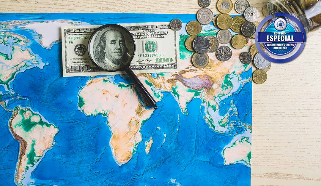World map under a magnifying glass focusing on a $100 bill with scattered coins and a blue logo stamp in the corner.