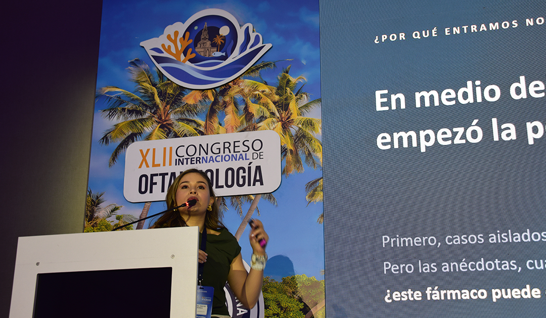 Woman speaking at a podium during a medical conference with a tropical-themed banner reading XLII Congreso Internacional de Oftalmología behind her.