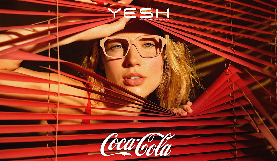 Promotional Coca-Cola ad showing a woman peeking through red blinds wearing pink glasses.