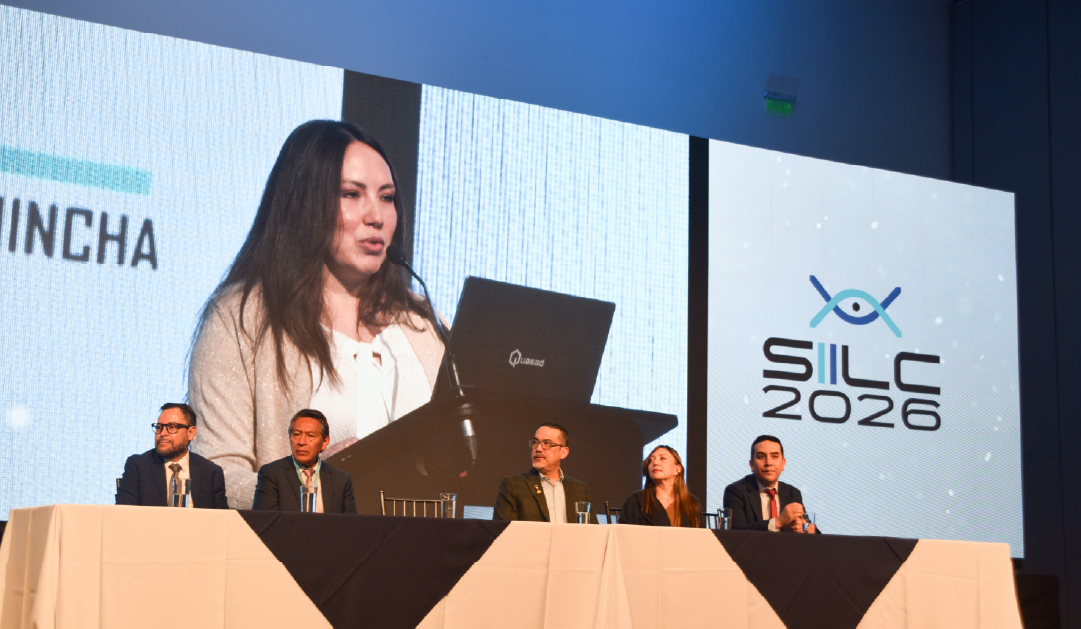 Panel of five people seated at a long table on a stage, large screen behind showing a speaker at a podium and the SILC 2026 logo.