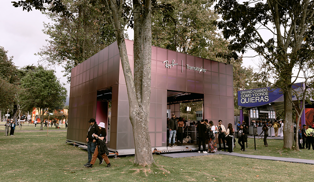 Pink metallic pavilion labeled Ray-Ban Transitions in a park, with people gathering inside and in line outside.