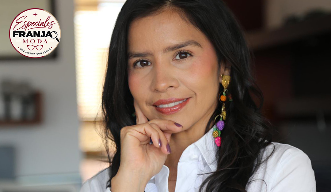 Portrait of a woman with long dark hair in a white shirt, resting her chin on her hand, wearing colorful dangling earrings; brand logo top-left corner.
