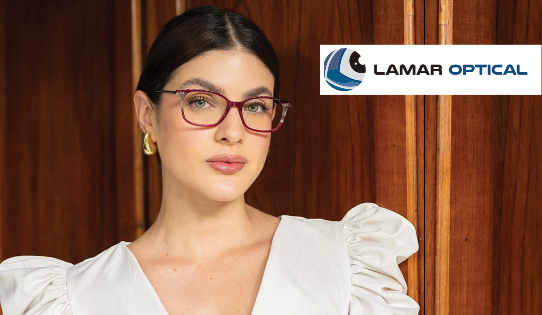 Woman wearing red-framed glasses posed against wood paneling with a Lamar Optical logo in the top-right corner.